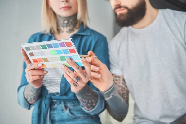 Cropped shot of young tattooed couple holding palette of colors and choosing color for home improvement — Stock Photo