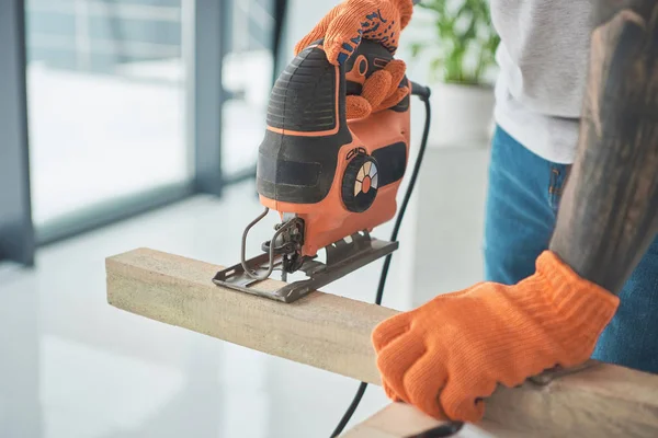 Close-up partial view of of young tattooed man using electric jigsaw during home improvement — Stock Photo