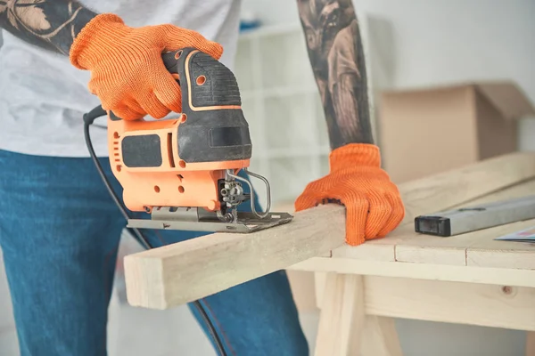 Close-up partial view of of young tattooed man using electric jigsaw — Stock Photo