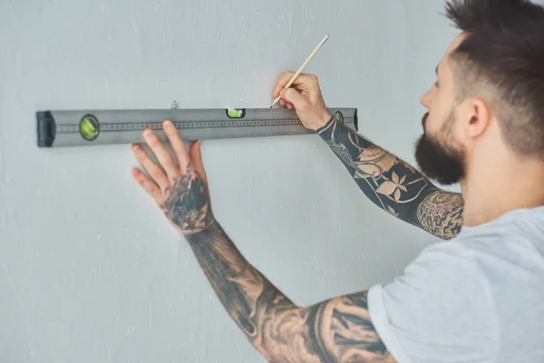 Cropped shot of young man holding level tool and marking wall with pencil during repairs — Stock Photo