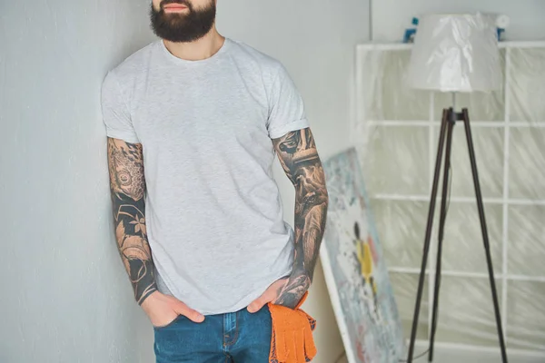 Colpo ritagliato di uomo tatuato barbuto appoggiato al muro in una nuova casa — Foto stock