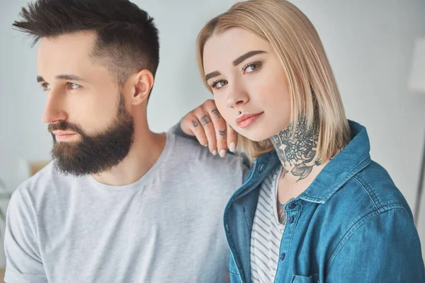 Beautiful tattooed girl standing with boyfriend and looking at camera — Stock Photo