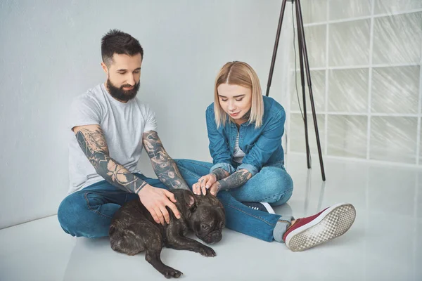 Happy young couple sitting and playing with french bulldog in new house — Stock Photo