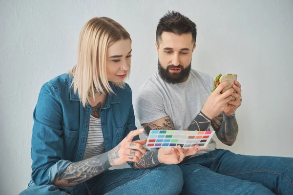 Menina segurando paleta de cores e homem comendo sanduíche na nova casa — Fotografia de Stock