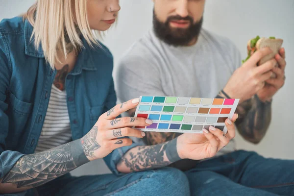 Cropped shot of girl holding color palette and man eating sandwich in new house — Stock Photo