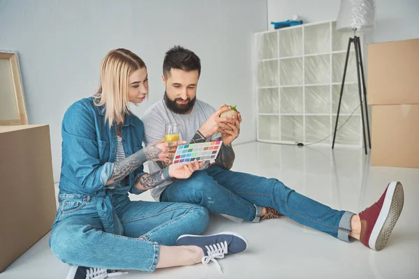 Couple with glass of juice and sandwich choosing colors on color pallette for new home — Stock Photo