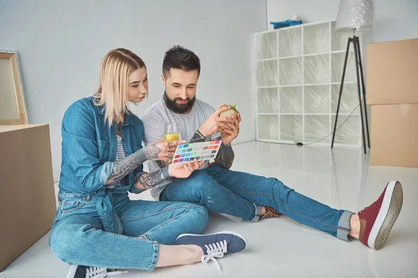 Couple avec verre de jus et sandwich choisir les couleurs sur la palette de couleurs pour la nouvelle maison — Photo de stock