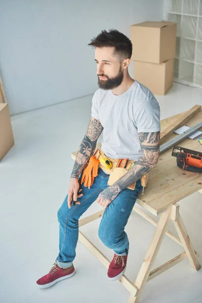 High angle view of bearded repairman with tattoos and tools leaning on wooden surface in new apartment — Stock Photo