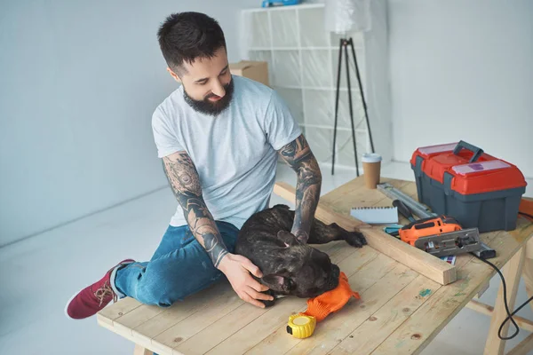 Tatuado homem jogar com francês bulldog na superfície de madeira no novo apartamento — Fotografia de Stock