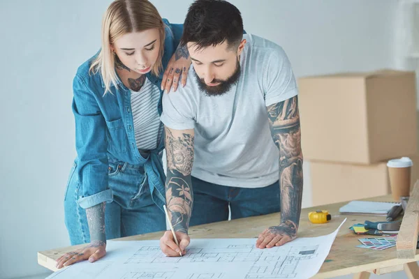 Ritratto di coppia tatuata che guarda cianografie su un tavolo di legno nella nuova casa — Foto stock