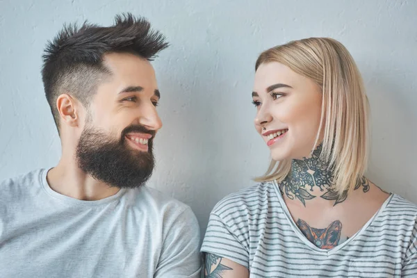 Retrato de pareja sonriente con tatuajes mirándose - foto de stock