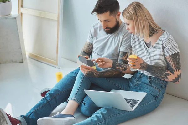 Young couple with glasses of juice and laptop choosing color on palette at new home — Stock Photo