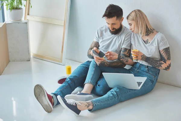 Jovem casal com copos de suco e laptop escolhendo cor na paleta na nova casa — Fotografia de Stock