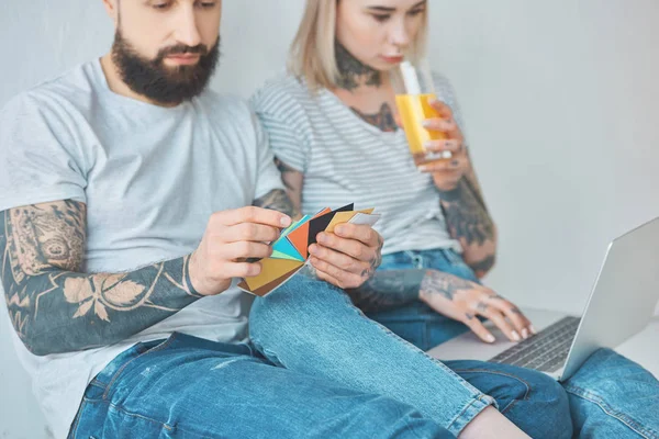 Enfoque selectivo del hombre barbudo elegir el color en la paleta con la novia beber jugo cerca en el nuevo apartamento - foto de stock