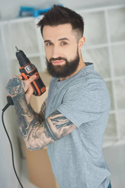 Retrato de homem tatuado com arma de parafuso nas mãos em novo apartamento — Fotografia de Stock