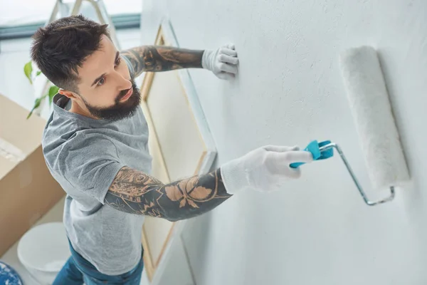 Seitenansicht tätowierter Reparaturarbeiter bemalt Wand in neuer Wohnung — Stockfoto