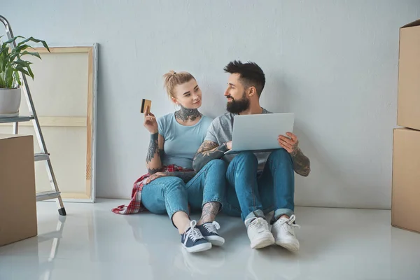 Couple souriant avec ordinateur portable et achats par carte de crédit en ligne à la nouvelle maison — Photo de stock