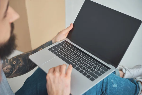 Partial view of tattooed man using laptop with blank screen in new apartment — Stock Photo