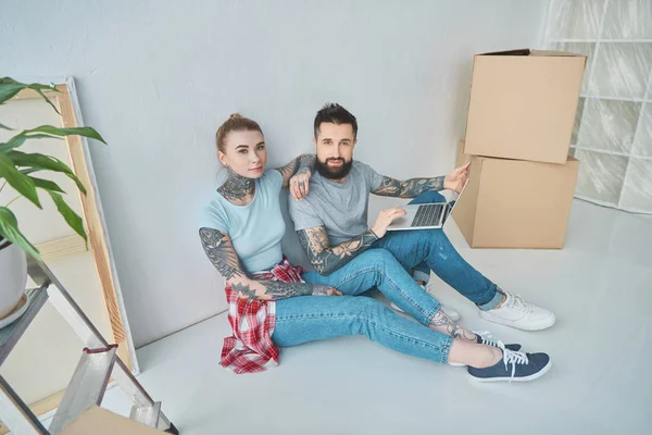 Молода пара з ноутбуком сидить на підлозі в новому будинку — стокове фото