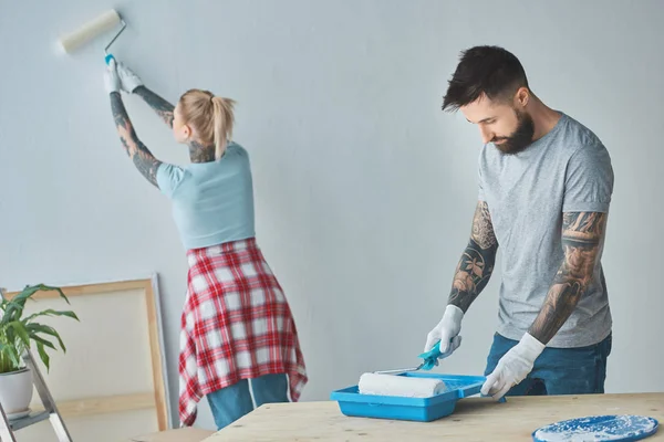 Casal tatuado com pincéis de pintura de rolo fazendo reparos em casa no novo apartamento — Fotografia de Stock