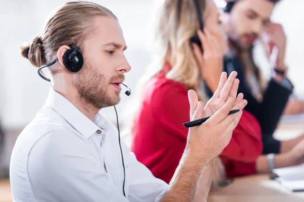 Enfoque selectivo de los operadores de centros de llamadas en auriculares con portátiles que trabajan en el lugar de trabajo en la oficina - foto de stock