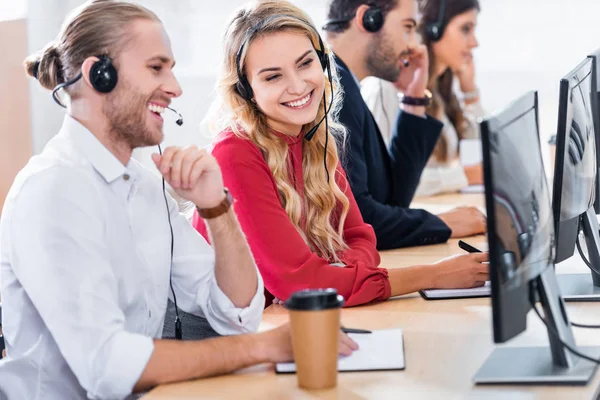 Focus selettivo di operatori di call center sorridenti che lavorano sul posto di lavoro con caffè da andare in ufficio — Foto stock