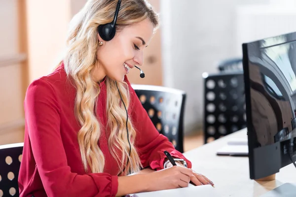 Side view of beautiful female call center operator in headset at workplace in office — Stock Photo