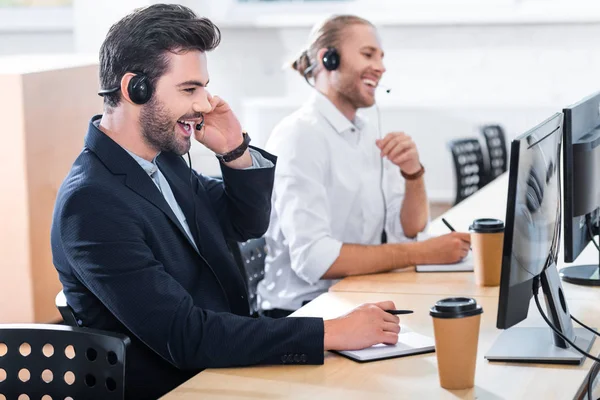 Visão lateral de operadores de call center masculinos em fones de ouvido no local de trabalho no escritório — Fotografia de Stock