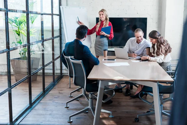 Mujer de negocios señalando a la pizarra blanca vacía durante la reunión en la oficina - foto de stock