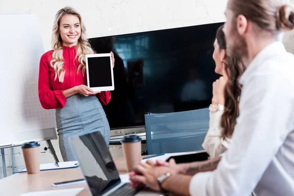 Улыбающаяся деловая женщина показывает планшет с чистым экраном коллегам во время встречи в офисе — стоковое фото
