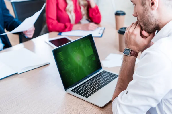 Visão parcial do empresário pensativo olhando para a tela do laptop no local de trabalho com papéis e colegas por perto — Fotografia de Stock