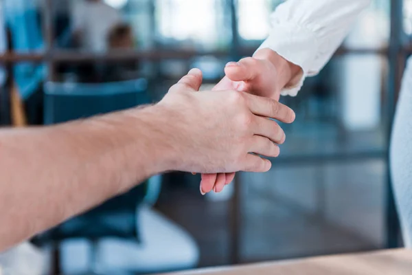 Recortado disparo de socios de negocios estrechando la mano en la oficina - foto de stock