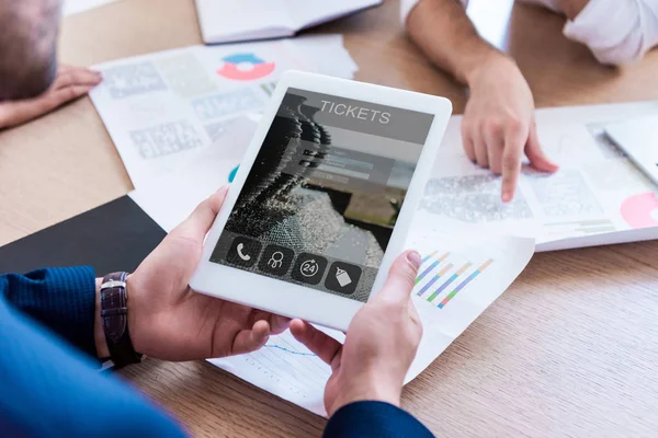 Teilansicht eines Geschäftsmannes, der während einer Besprechung im Büro ein Tablet mit Ticketaufdruck auf dem Bildschirm hält — Stockfoto