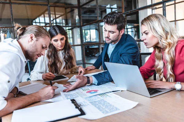 Equipo de negocios discutiendo nuevo proyecto de negocio en el lugar de trabajo con papeles y portátil en la oficina - foto de stock