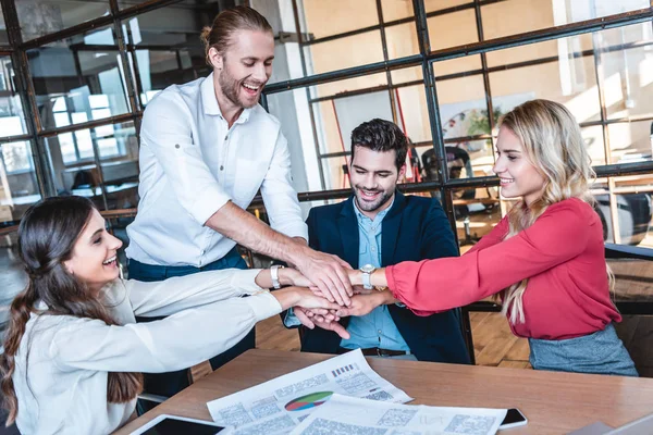 Happy business team holding hands at workplace in office — Stock Photo