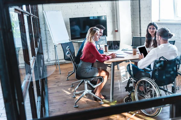 Young handicapped businessman in wheelchair working with colleagues in office — Stock Photo