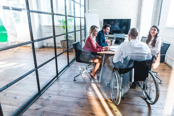 Young disabled businessman in wheelchair working with colleagues in office — Stock Photo