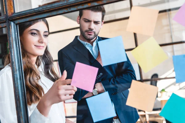 Young businessman and businesswoman looking at colorful sticky notes at workplace — Stock Photo