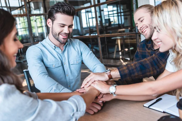 Jóvenes colegas de negocios felices apilando manos en el lugar de trabajo - foto de stock