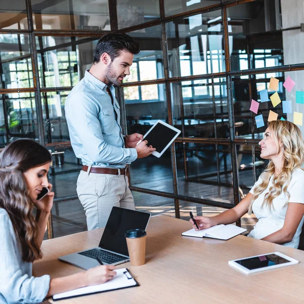 Jungunternehmer nutzt digitales Tablet und schaut lächelnde Kollegin am Arbeitsplatz an — Stockfoto