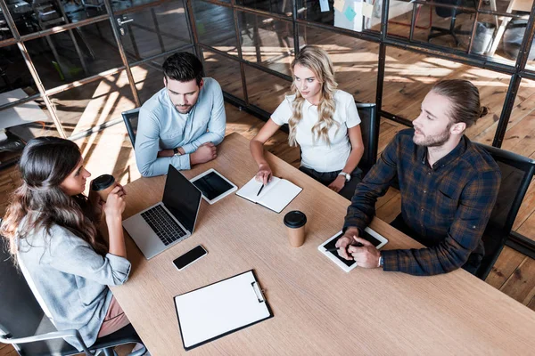 Vista de ángulo alto de los compañeros de trabajo jóvenes discutiendo proyecto durante la reunión de negocios - foto de stock