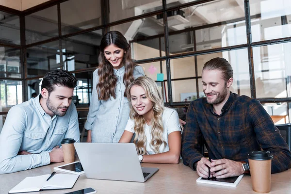 Les jeunes gens d'affaires souriants qui travaillent avec un ordinateur portable sur le lieu de travail — Photo de stock