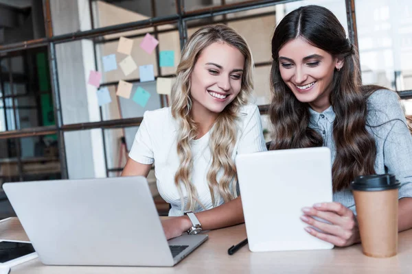 Jovens empresárias sorridentes que utilizam dispositivos digitais no local de trabalho — Fotografia de Stock