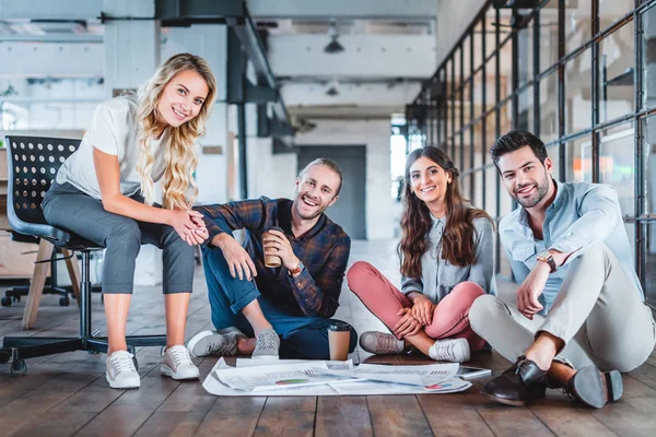 Счастливая молодая деловая команда, работающая с бумагами и улыбающаяся перед камерой в офисе — стоковое фото