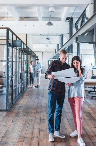 Smiling young business people looking at papers while standing together at workspace — Stock Photo