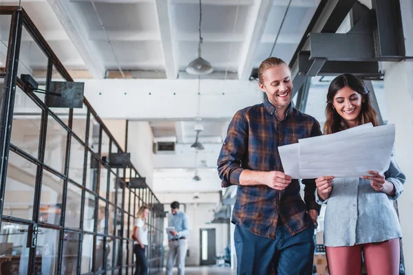Niedrigwinkel-Ansicht lächelnder junger Geschäftskollegen beim Betrachten von Papieren, während sie gemeinsam am Arbeitsplatz stehen — Stockfoto