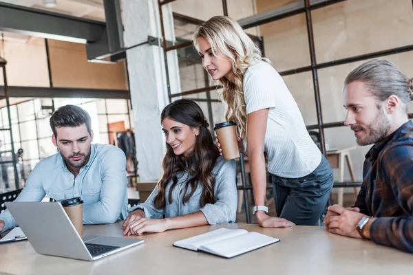 Smiling young coworkers using laptop together in office — Stock Photo