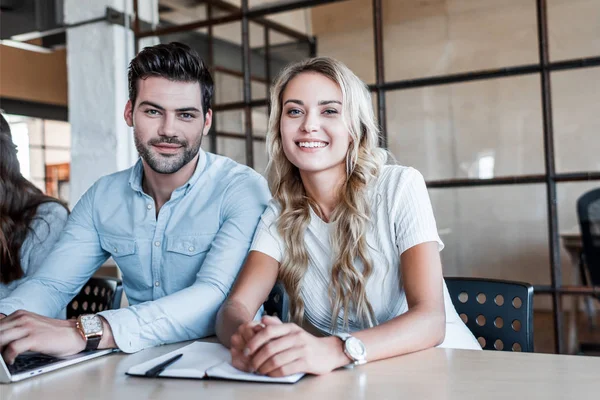 Happy young business colleagues sitting together and smiling at camera in office — Stock Photo