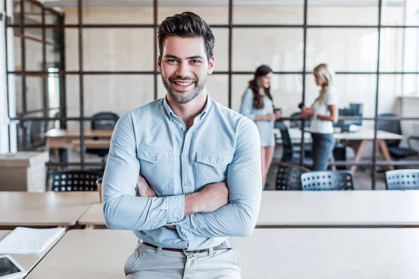 Jovem empresário bonito com braços cruzados sorrindo para a câmera no escritório — Fotografia de Stock