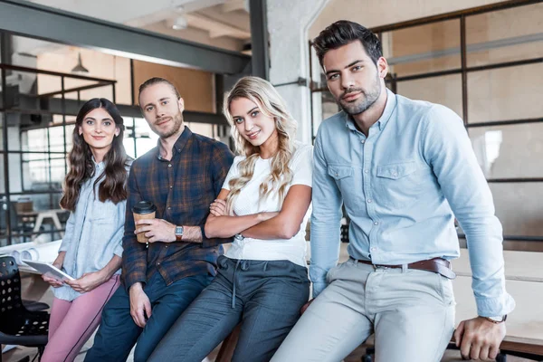 Jóvenes profesionales de negocios sentados y sonriendo a la cámara en la oficina - foto de stock